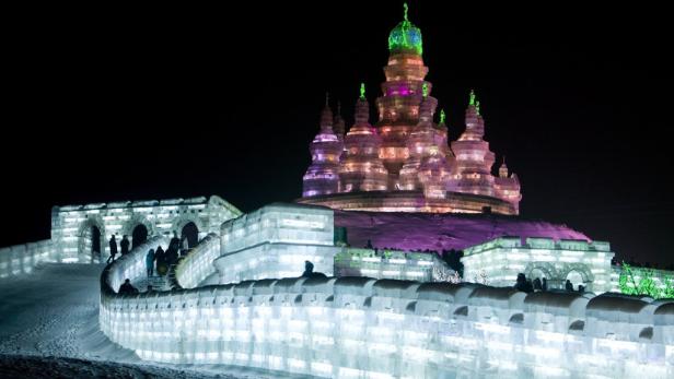 Eine beleuchtete Eisburg mit Menschen bei Nacht.