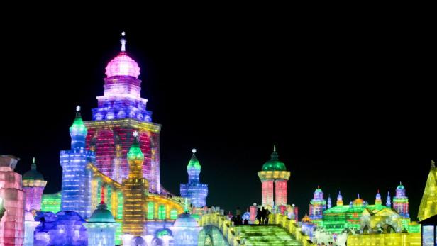 Eine farbenfrohe Eisburg mit vielen Lichtern und Menschen im Harbin International Ice and Snow Sculpture Festival.