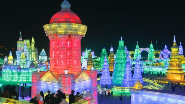 Illuminierte Eisstrukturen und Menschen auf dem Harbin International Ice and Snow Sculpture Festival.