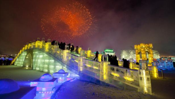 Menschen besuchen eine beleuchtete Eisbrücke während eines Feuerwerks.
