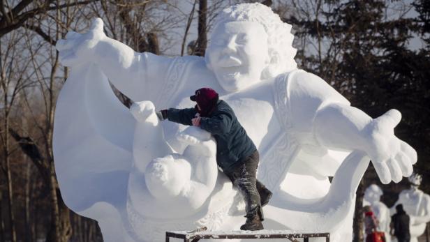 Eine Person arbeitet an einer großen Schneeskulptur im Freien.