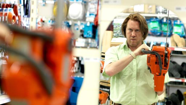 Ein Mann im Baumarkt betrachtet eine orangefarbene Kettensäge.