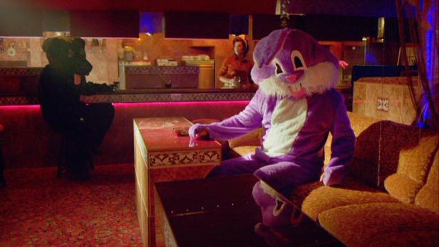 Ein Mann im lila Hasenkostüm sitzt in einer Bar.