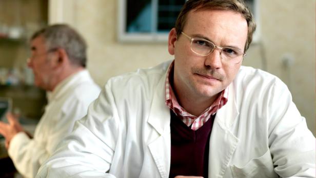 Ein Arzt mit Brille und Schnurrbart blickt in die Kamera.