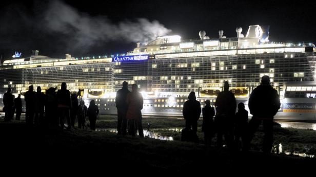 Eine Menschengruppe beobachtet nachts ein beleuchtetes Kreuzfahrtschiff von Royal Caribbean.