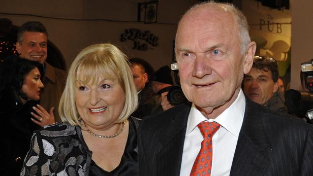 Ein älterer Mann mit Krawatte und eine Frau mit Halskette lächeln in die Kamera.