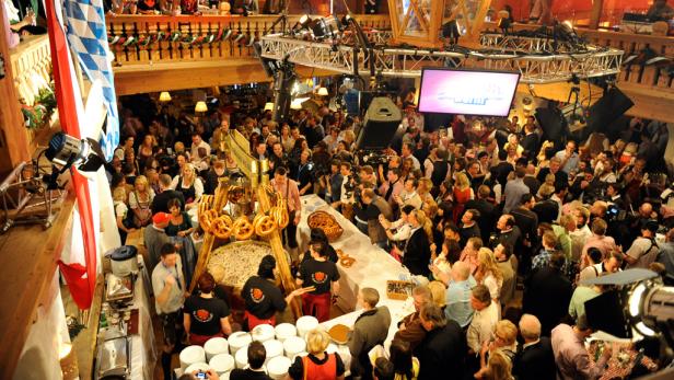 Eine Menschenmenge in einem Festzelt mit bayerischer Dekoration und Brezeln.