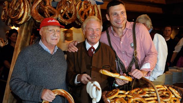 Drei Männer, darunter Vitali Klitschko in Tracht, posieren mit Brezeln und Weißwürsten.
