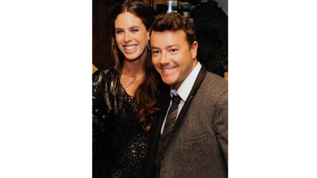 Eine lächelnde Frau in Paillettenjacke posiert mit einem Mann im Tweed-Sakko.