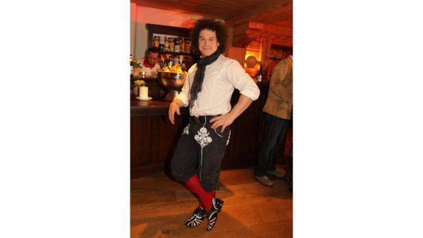 Ein Mann in Tracht posiert in einer Bar mit roten Socken und auffälligen Schuhen.