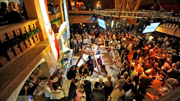 Eine große Menschenmenge in Tracht feiert in einem hölzernen Saal mit bayerischen Flaggen.