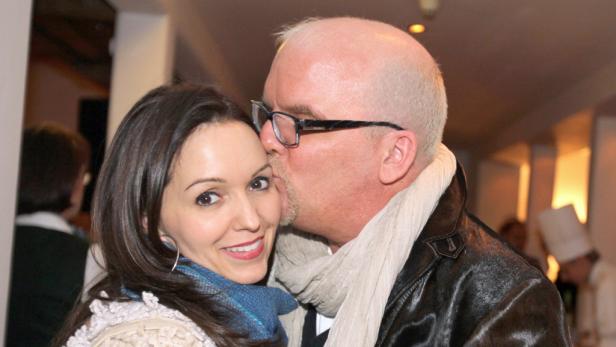 Ein Mann mit Brille gibt einer lächelnden Frau einen Kuss auf die Wange.