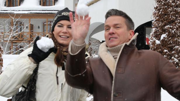 Ein Mann und eine Frau werfen im Winter Schneebälle vor einem schneebedeckten Haus.