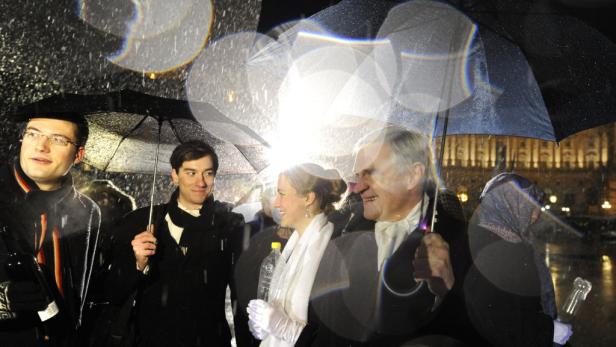 Eine Gruppe von Menschen mit Regenschirmen steht im Regen vor einem Gebäude.