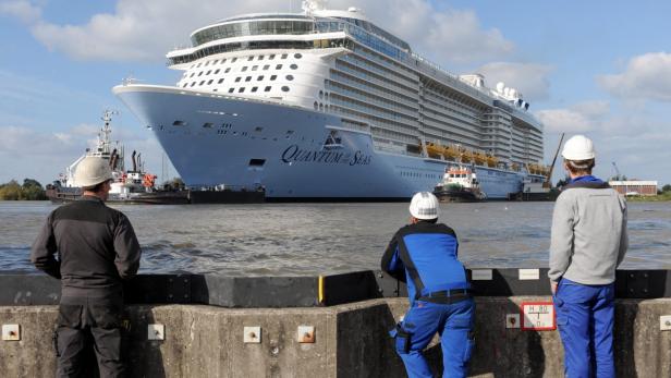 Drei Bauarbeiter beobachten das Kreuzfahrtschiff „Quantum of the Seas“ im Hafen.