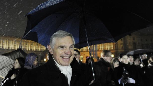 Ein lächelnder Mann steht im Regen unter einem Regenschirm.
