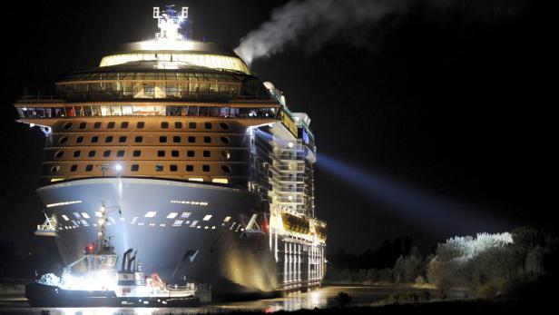 Ein großes Kreuzfahrtschiff wird nachts von einem Schlepper begleitet.