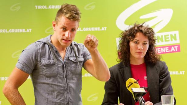 Zwei Personen stehen vor einem grünen Hintergrund mit dem Logo der Tiroler Grünen.