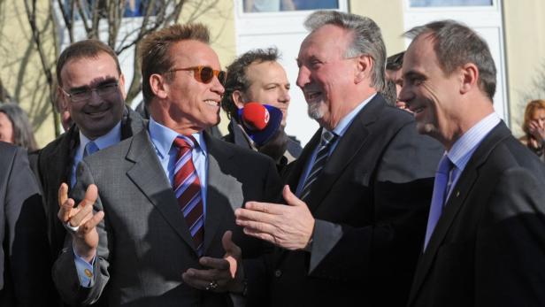 Arnold Schwarzenegger unterhält sich mit anderen Männern im Anzug.