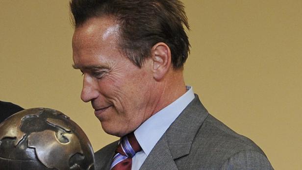 Arnold Schwarzenegger betrachtet eine Weltkugel.