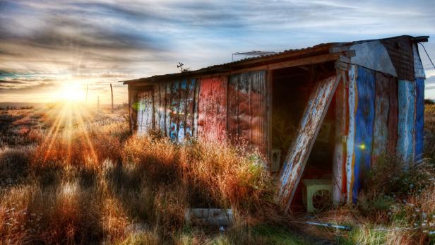 Eine baufällige Hütte steht in einem Feld im goldenen Licht der Abendsonne.
