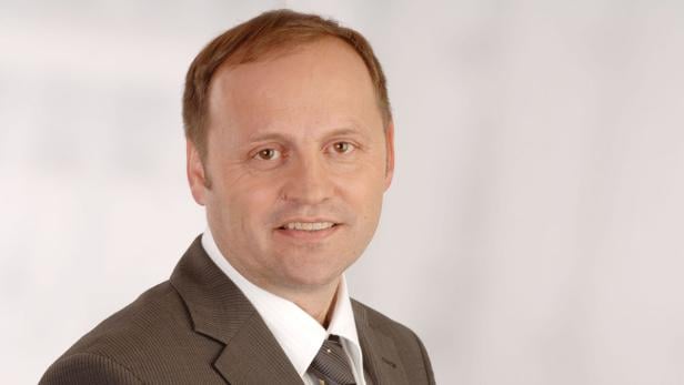 Ein Mann mit braunen Haaren und Anzug lächelt in die Kamera.