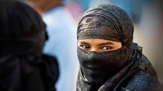 Eine Frau mit einem schwarzen Hidschab blickt in die Kamera.