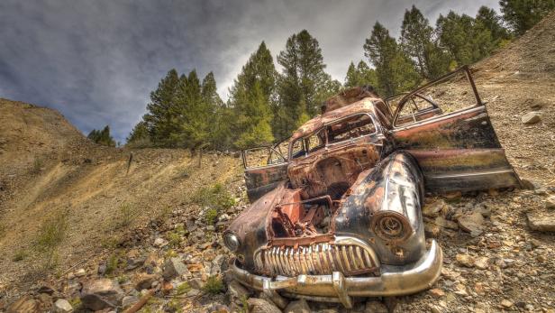 Ein verrostetes, zerstörtes Auto steht auf einem felsigen Hügel.