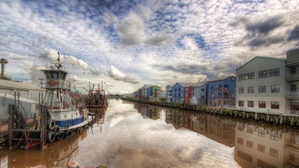 Ein Schlepper liegt an einem Kanal mit bunten Häusern unter einem bewölkten Himmel.