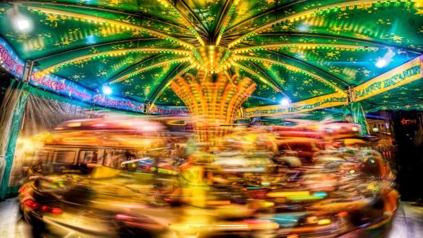 Ein Karussell dreht sich schnell auf einem Jahrmarkt, Lichter ziehen verschwommene Spuren.