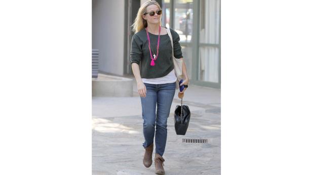 Reese Witherspoon geht mit Sonnenbrille, Jeans und Stiefeln die Straße entlang.