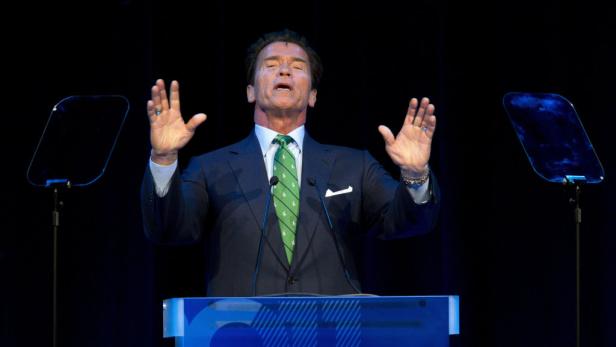 Arnold Schwarzenegger gestikuliert bei einer Rede auf einer Bühne.