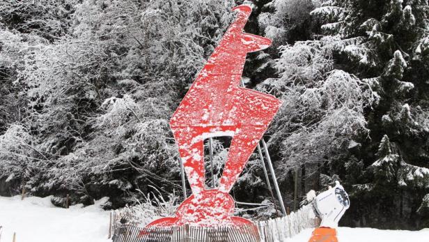 Eine rote Hirschskulptur steht verschneit vor einem Winterwald.