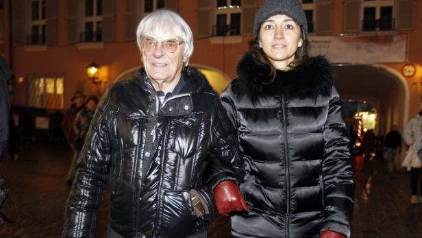 Bernie Ecclestone mit einer Frau in Winterkleidung auf einer abendlichen Straße.