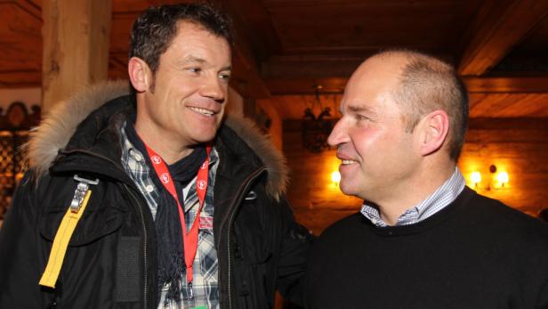 Zwei Männer unterhalten sich lächelnd in einem holzgetäfelten Raum.