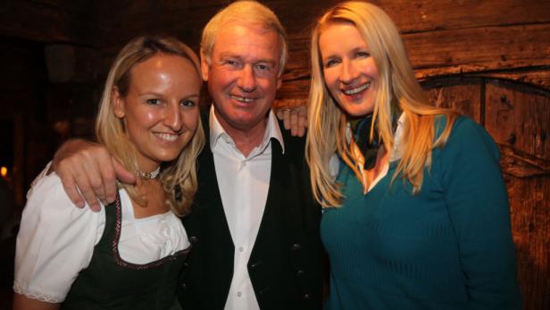 Drei lächelnde Personen posieren vor einer Holzwand.