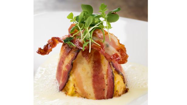 Ein Gericht mit Speck umwickelt und mit frischen Kräutern garniert, serviert in einer hellen Soße.