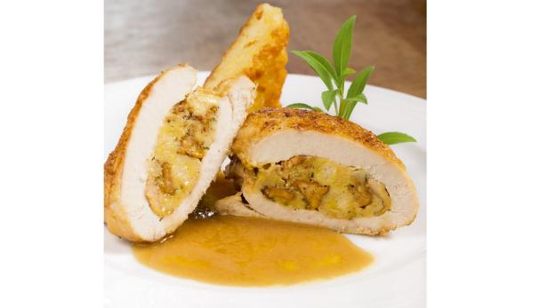 Gefüllte Hähnchenbrust mit Soße und einem Kartoffelstück auf einem Teller.