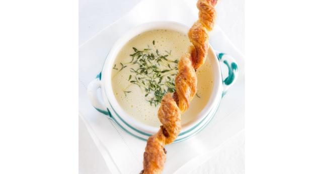 Eine Schüssel cremige Suppe, garniert mit frischen Kräutern und einer Gebäckstange.