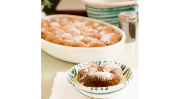 Eine Schüssel mit Germknödeln in Vanillesauce, bestäubt mit Puderzucker.