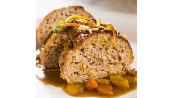 Ein aufgeschnittener Hackbraten mit Gemüse und Soße auf einem Teller.