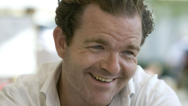 Ein lächelnder Mann mit hellbraunen Haaren und einem weißen Hemd.