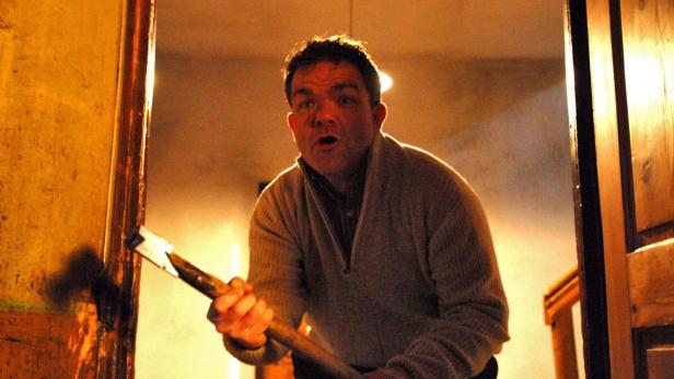 Ein Mann steht mit einer Axt in der Hand in einer Türöffnung.