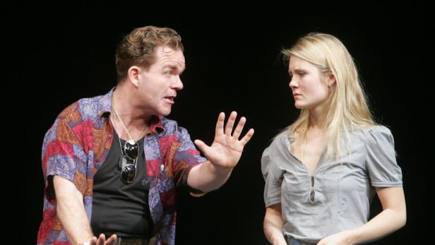 Ein Mann gestikuliert aufgeregt, während eine blonde Frau ihn aufmerksam ansieht.