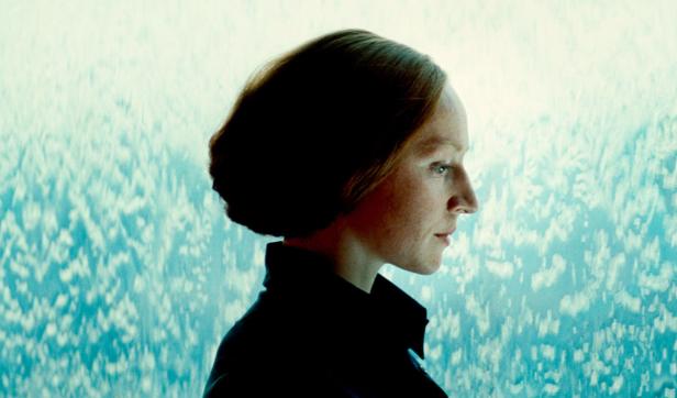 Eine Frau mit kurzen, dunklen Haaren im Profil vor einem hellblauen Hintergrund.