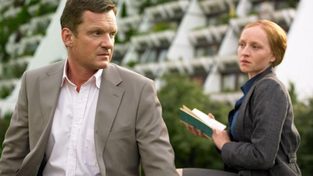 Ein Mann im Anzug und eine Frau mit einem Buch vor einem Gebäude.