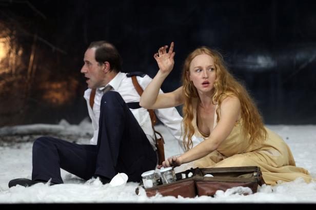 Eine Frau in einem hellen Kleid und ein Mann in Uniform sitzen auf einer Bühne mit Kunstschnee.