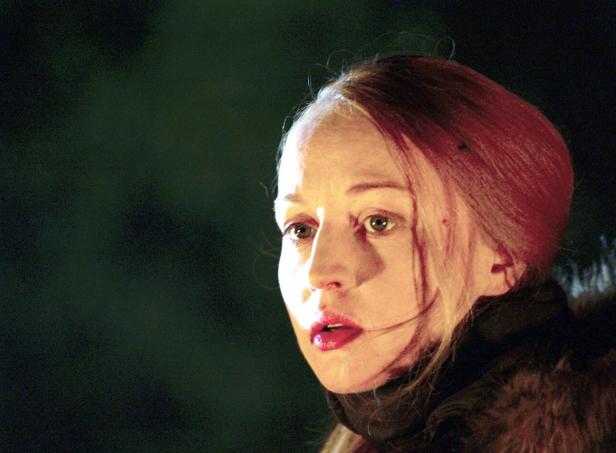 Das Porträt einer Frau mit roten Haaren und roten Lippen vor dunklem Hintergrund.