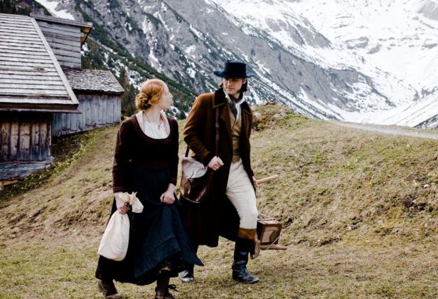 Eine Frau und ein Mann in historischer Kleidung wandern in den Bergen.