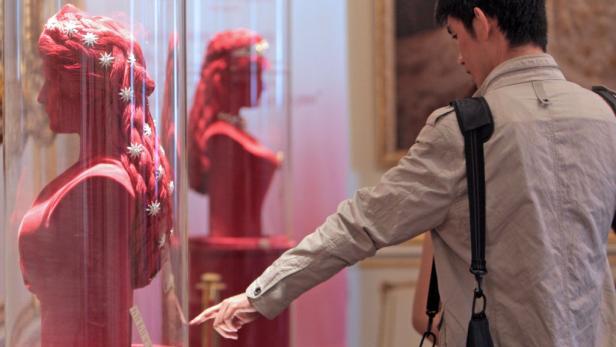 Ein Mann betrachtet eine rote Büste mit Sternen im Haar in einem Museum.